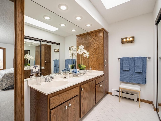 ensuite bathroom with a baseboard heating unit, a skylight, and a sink