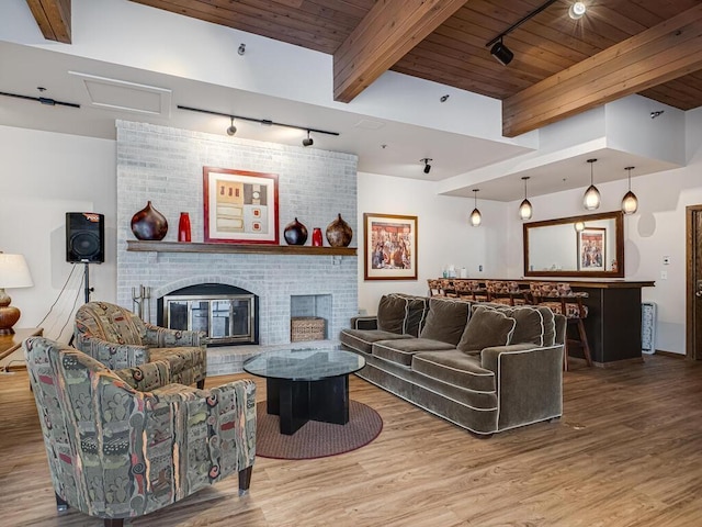 living area featuring beam ceiling, wooden ceiling, wood finished floors, and a brick fireplace