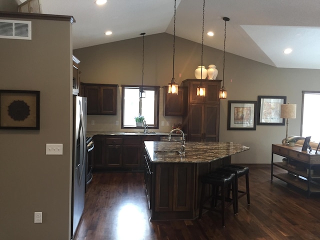 kitchen featuring an island with sink, dark wood-type flooring, stone countertops, hanging light fixtures, and vaulted ceiling