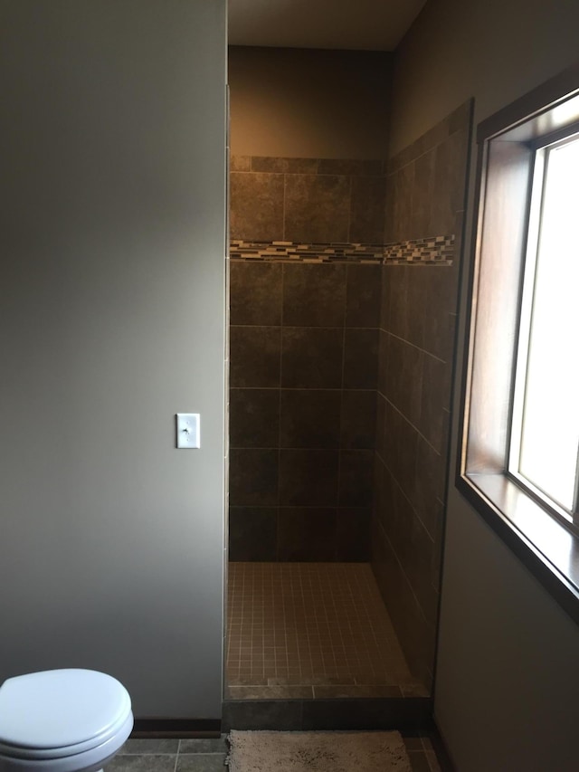 bathroom with toilet, tile patterned floors, and a tile shower