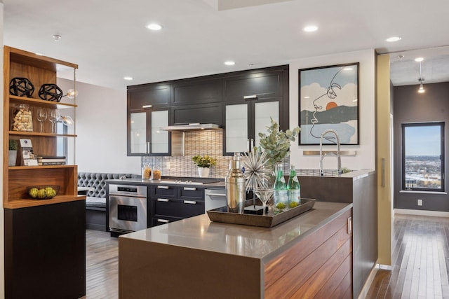 kitchen featuring appliances with stainless steel finishes, hanging light fixtures, light wood-type flooring, and tasteful backsplash