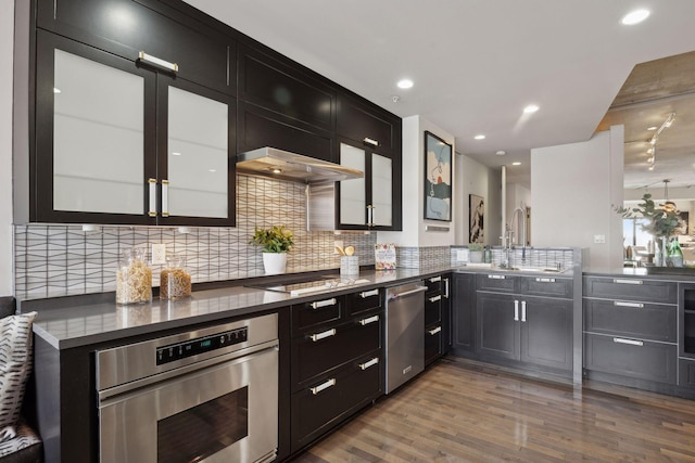 kitchen featuring stainless steel appliances, sink, wall chimney exhaust hood, tasteful backsplash, and kitchen peninsula