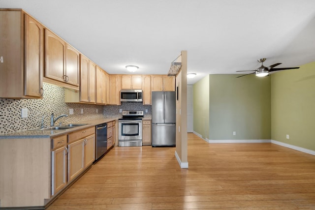 kitchen featuring stainless steel appliances, tasteful backsplash, light wood-style flooring, a sink, and baseboards