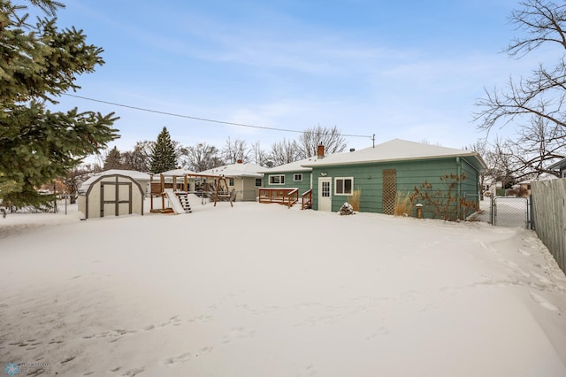 snow covered rear of property featuring a wooden deck and a storage unit