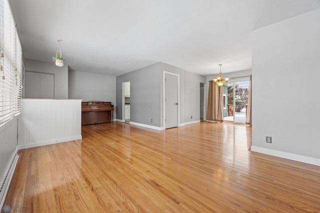 unfurnished living room with a healthy amount of sunlight, baseboard heating, light wood-type flooring, and an inviting chandelier