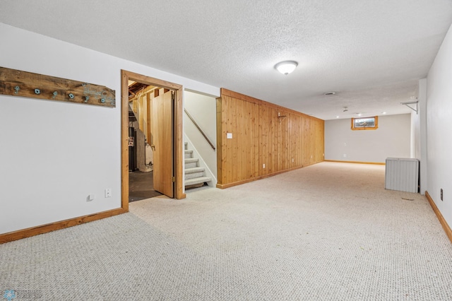 basement with wooden walls, radiator heating unit, a textured ceiling, and light colored carpet