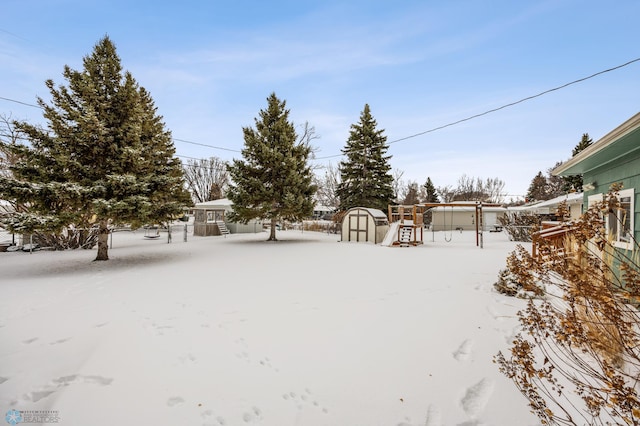 snowy yard featuring a playground and a storage shed