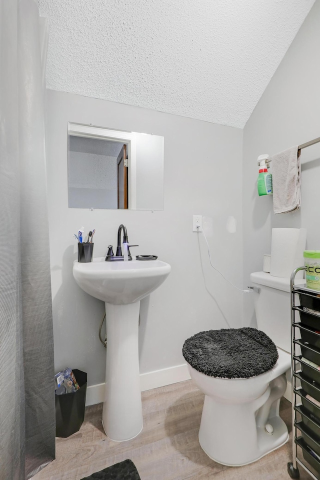 bathroom featuring hardwood / wood-style flooring, toilet, vaulted ceiling, and a textured ceiling