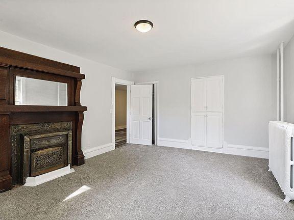 203 4th St, River Falls, WI 54022 - unfurnished living room featuring baseboards, a fireplace with flush hearth, and carpet