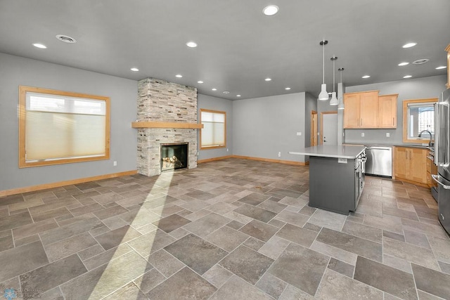 kitchen with a stone fireplace, a center island, hanging light fixtures, light brown cabinets, and stainless steel appliances