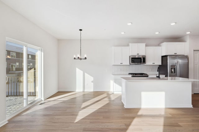 kitchen featuring pendant lighting, an island with sink, white cabinetry, stainless steel appliances, and light wood-type flooring