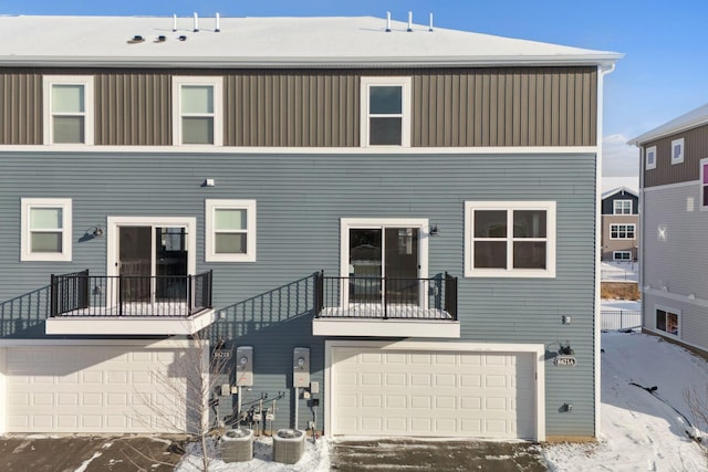 snow covered property featuring cooling unit, a balcony, and a garage