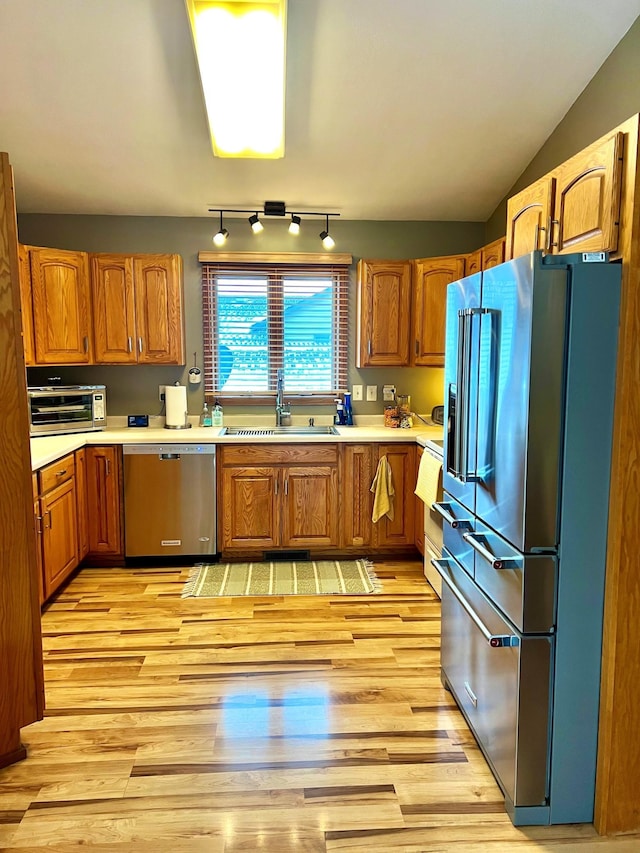 kitchen featuring stainless steel appliances, lofted ceiling, sink, and light hardwood / wood-style flooring