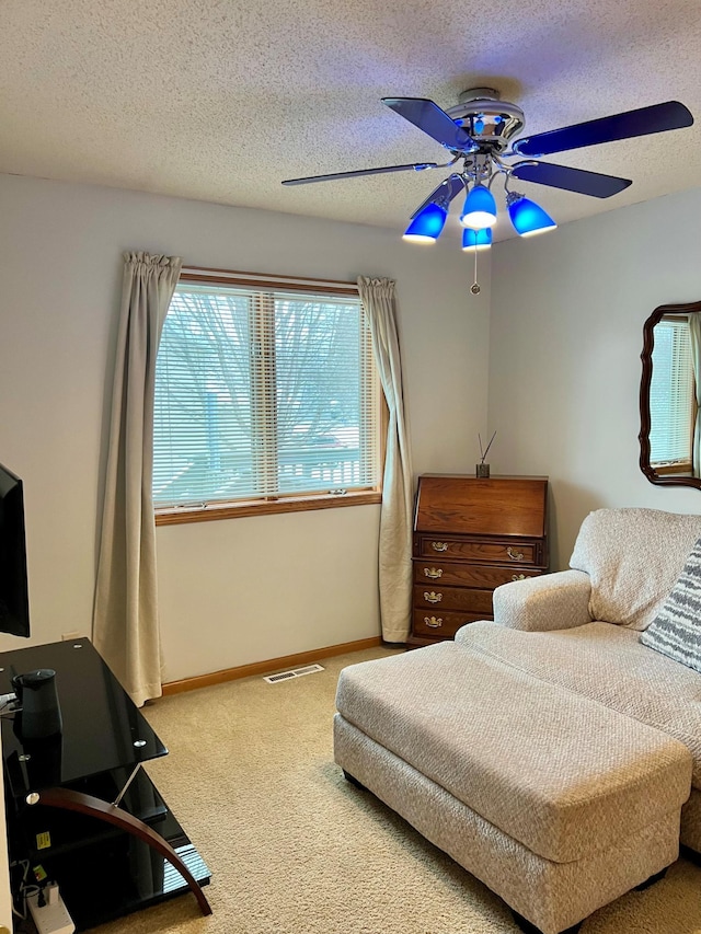 living area featuring ceiling fan, carpet floors, and a textured ceiling