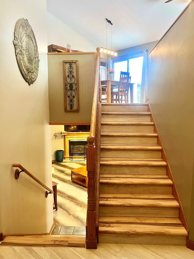 stairs featuring hardwood / wood-style floors, a fireplace, and vaulted ceiling