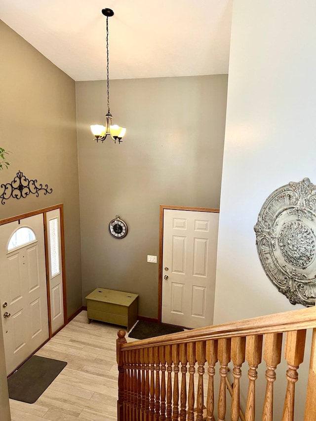 entryway featuring light wood-style floors, a chandelier, a towering ceiling, and baseboards