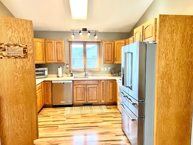 kitchen featuring stainless steel appliances, a sink, light wood-style flooring, vaulted ceiling, and light countertops