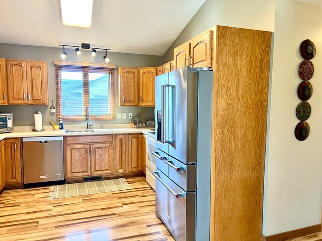 kitchen with appliances with stainless steel finishes, a sink, light wood-style floors, light countertops, and vaulted ceiling