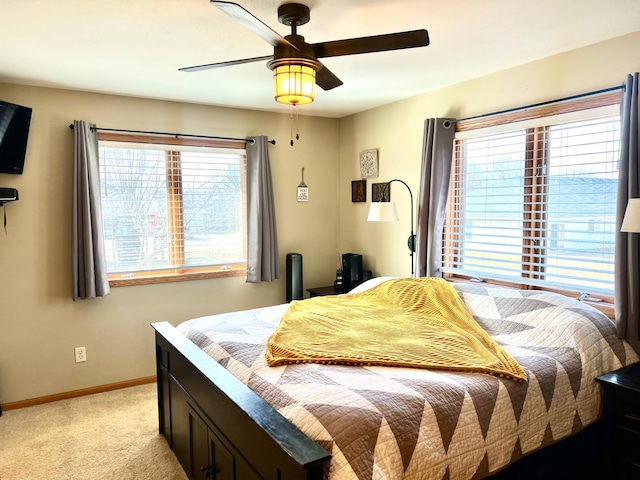 bedroom featuring multiple windows, baseboards, light carpet, and a ceiling fan