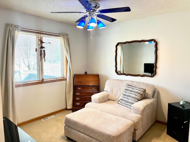 sitting room with light colored carpet, a ceiling fan, baseboards, and a textured ceiling