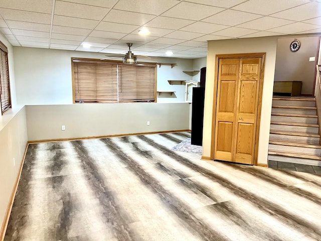 unfurnished living room with wood finished floors, a paneled ceiling, stairway, baseboards, and ceiling fan