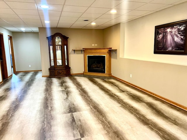 unfurnished living room featuring baseboards, a fireplace with raised hearth, and a paneled ceiling