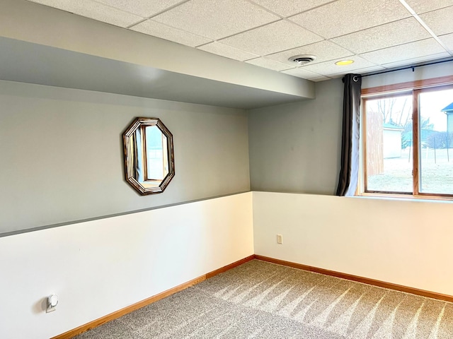 carpeted spare room featuring baseboards and a drop ceiling