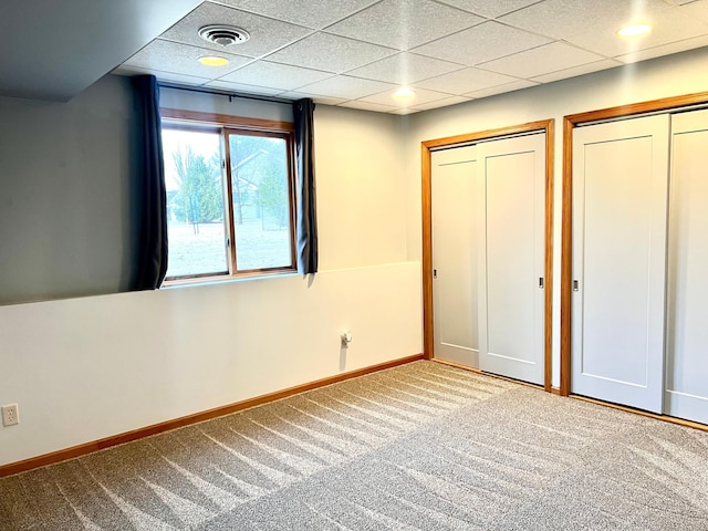 unfurnished bedroom featuring carpet flooring, multiple closets, baseboards, and a drop ceiling