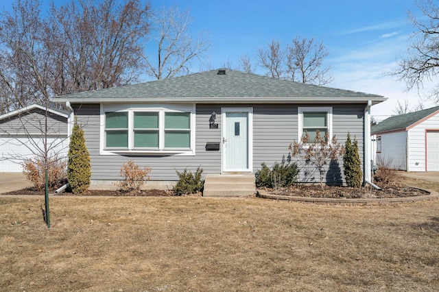 view of front of house with an outdoor structure, a detached garage, a front yard, and roof with shingles