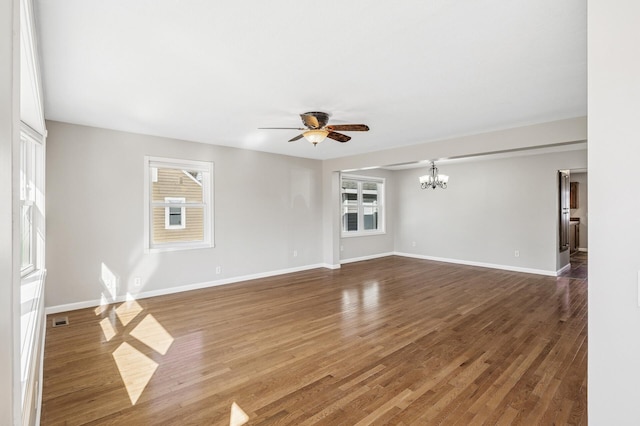 empty room with visible vents, ceiling fan with notable chandelier, baseboards, and wood finished floors