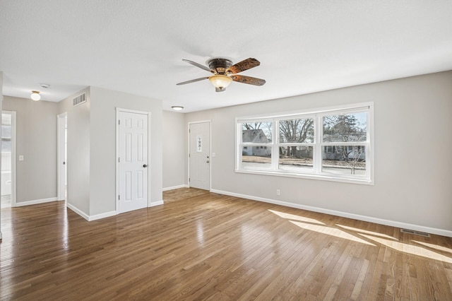 unfurnished living room with hardwood / wood-style flooring, baseboards, visible vents, and ceiling fan