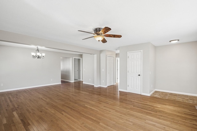 spare room featuring light wood finished floors, ceiling fan with notable chandelier, and baseboards