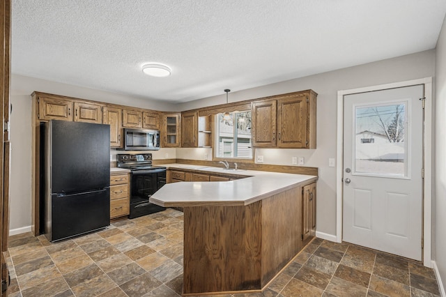 kitchen featuring baseboards, brown cabinets, a peninsula, stone finish floor, and black appliances