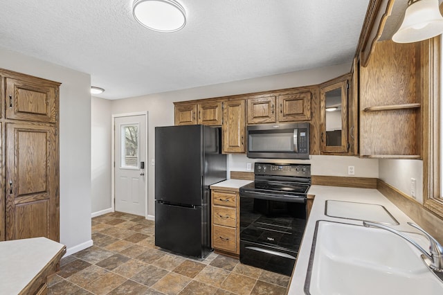 kitchen with baseboards, light countertops, brown cabinets, black appliances, and a sink