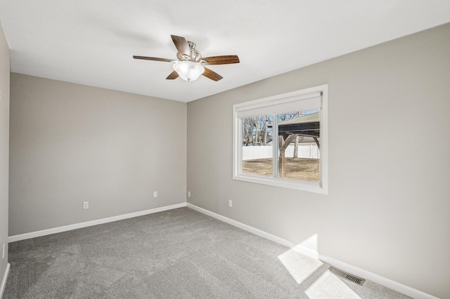 carpeted spare room with visible vents, baseboards, and a ceiling fan