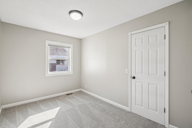 empty room featuring visible vents, baseboards, carpet, and a textured ceiling