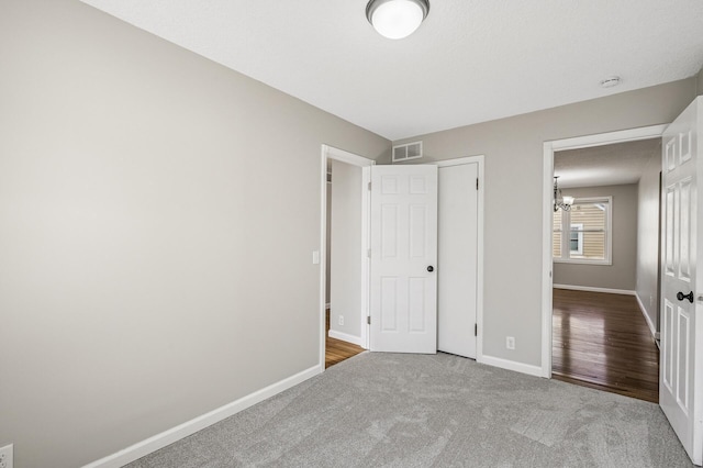 unfurnished bedroom with visible vents, baseboards, a notable chandelier, and carpet floors