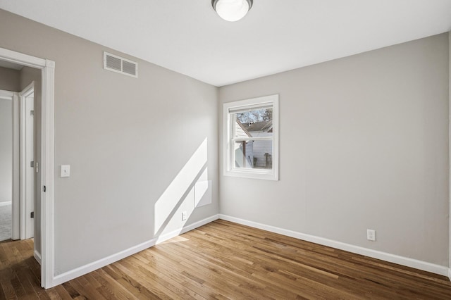 empty room featuring visible vents, baseboards, and wood finished floors