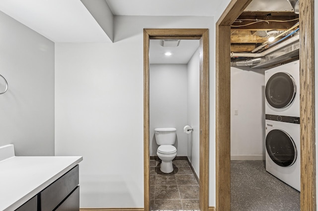 bathroom featuring stacked washer / drying machine, baseboards, and toilet