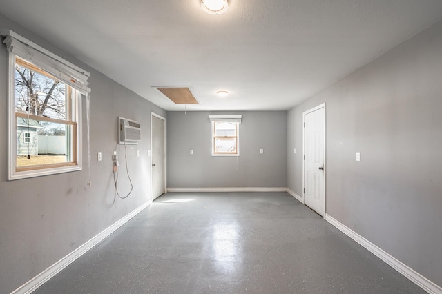 empty room with an AC wall unit, baseboards, attic access, and finished concrete floors