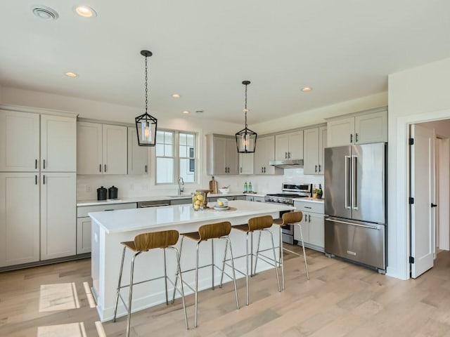 kitchen with light hardwood / wood-style flooring, a breakfast bar area, hanging light fixtures, a kitchen island, and appliances with stainless steel finishes