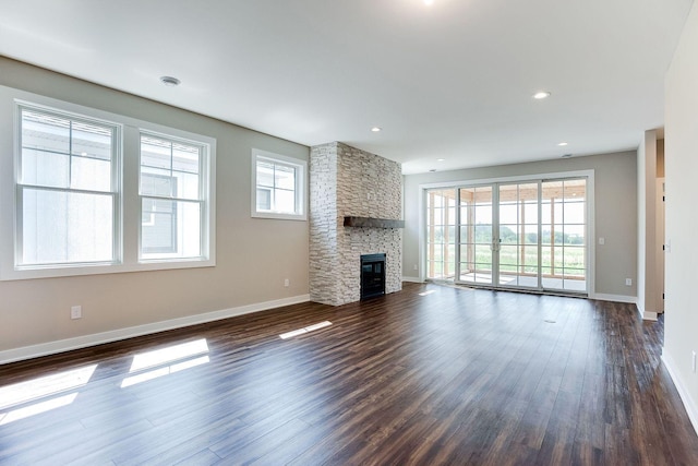 unfurnished living room featuring dark hardwood / wood-style flooring, plenty of natural light, and a stone fireplace