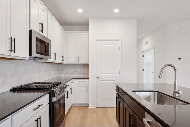 kitchen with appliances with stainless steel finishes, light wood-type flooring, dark brown cabinets, sink, and white cabinetry