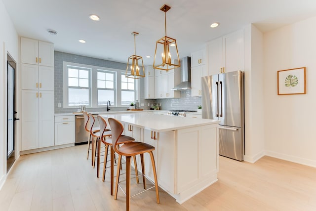 kitchen with white cabinets, stainless steel appliances, wall chimney range hood, and a kitchen island