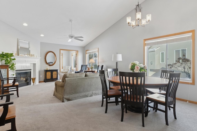 dining area with light carpet, ceiling fan with notable chandelier, plenty of natural light, and a tile fireplace