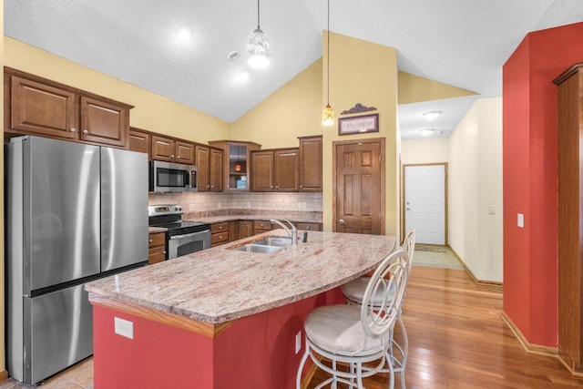 kitchen with appliances with stainless steel finishes, sink, backsplash, hanging light fixtures, and a kitchen island with sink