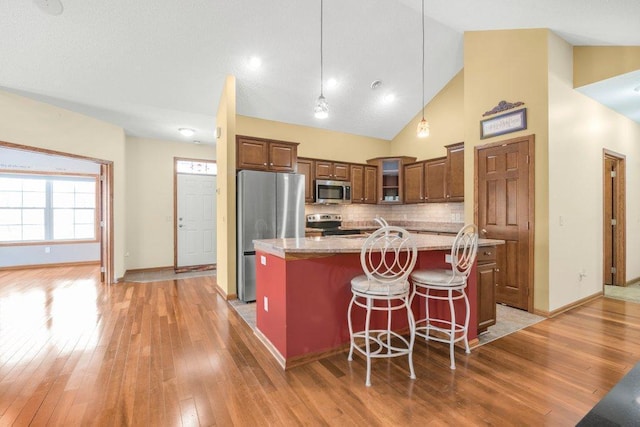 kitchen with pendant lighting, appliances with stainless steel finishes, an island with sink, light stone counters, and a breakfast bar