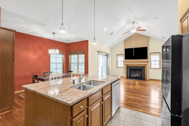 kitchen with dishwasher, sink, hanging light fixtures, black fridge, and a center island with sink