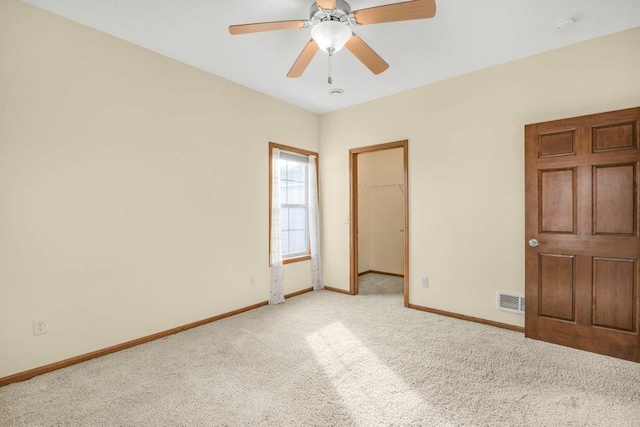 unfurnished bedroom featuring ceiling fan, a walk in closet, a closet, and light colored carpet