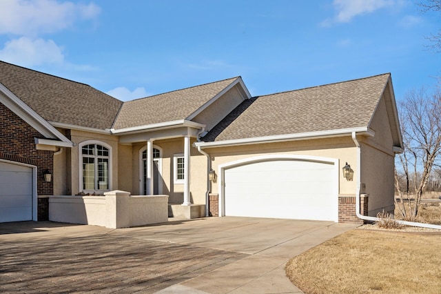 ranch-style house featuring brick siding, stucco siding, a shingled roof, an attached garage, and driveway